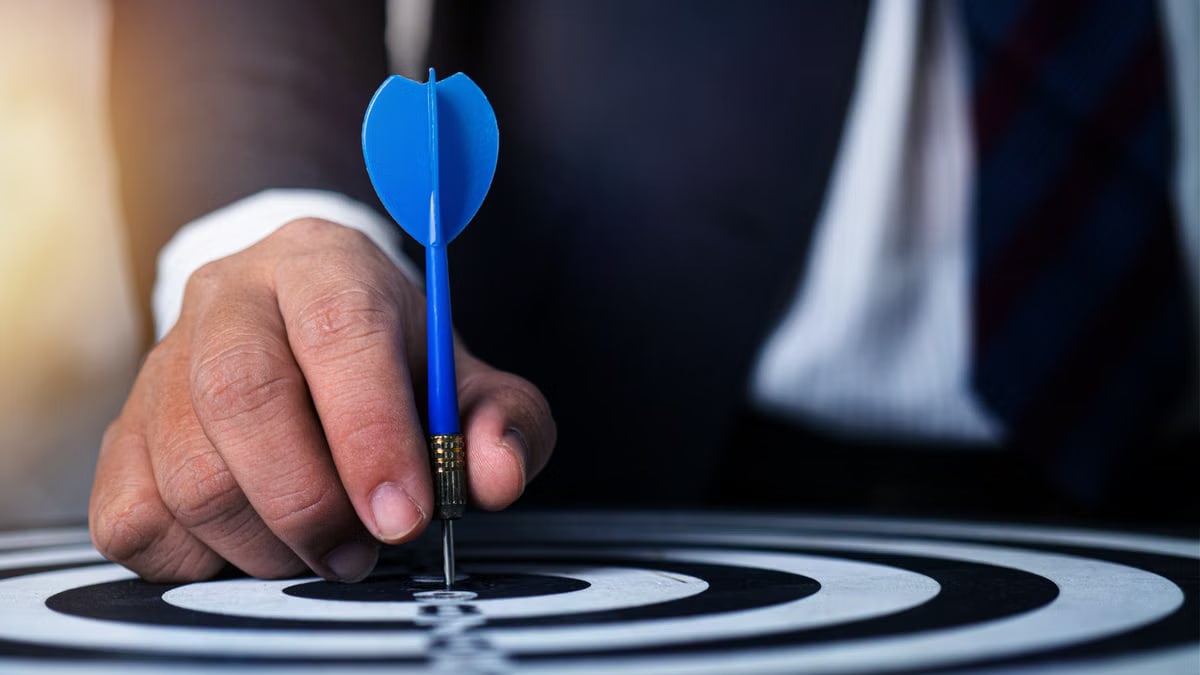 Close-up of a man's hand holding a blue dart on a bullseye, symbolizing precision and focus.